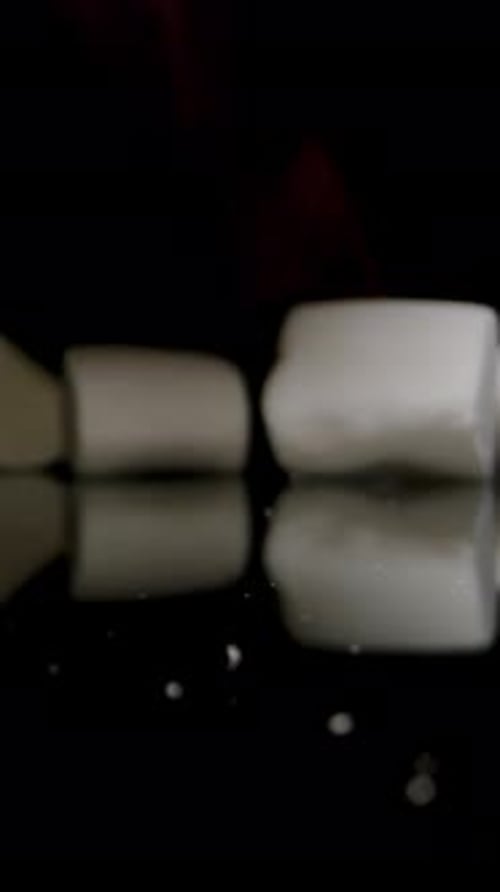 Vertical video. Hand Appears from Darkness and Throws a Handful of Marshmallows onto the Table.