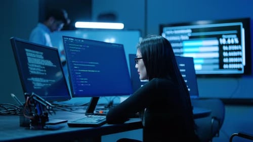 Junge asiatische Programmiererin schreibt Code auf mehreren Monitoren in einer dunklen Hightech-Cybersicherheit