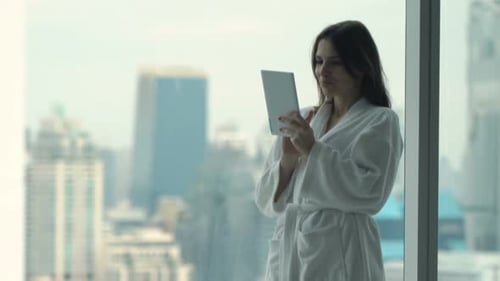 Woman in Robe Using Tablet by City View Window