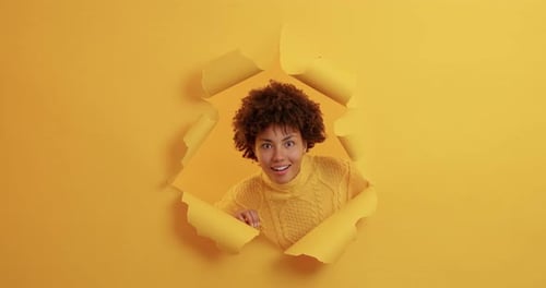 Woman Smiling Through Torn Paper on Yellow Background