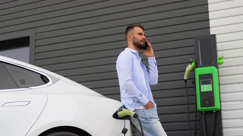 A Man Phoning While Charging Car at Electric Vehicle Charging Station