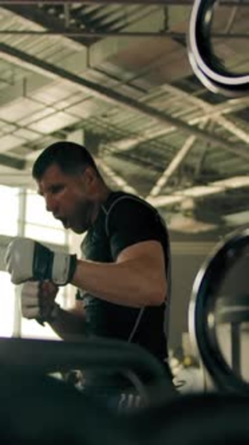 Vertical of Male in a Sportswear Hitting Hard on the Punching Bag in the Gym