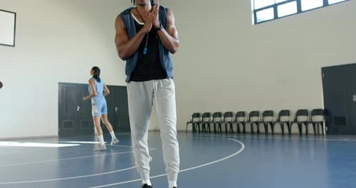 Coaching basketball, man smiling and walking on court, female player in background