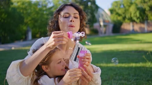 Child Mom Having Fun Blowing Colorful Soap Bubbles on Family Picnic Park Closeup