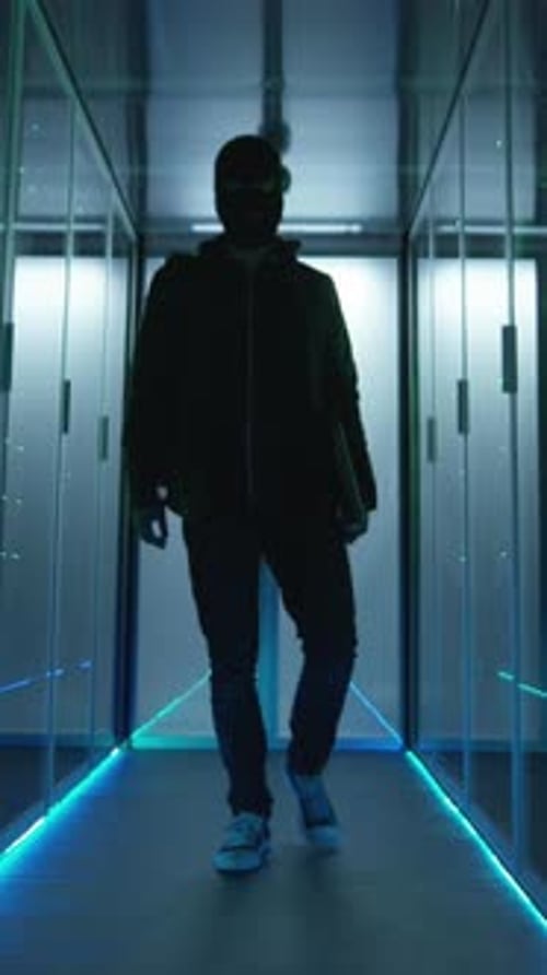 Masked Hacker Walking Through a Server Room