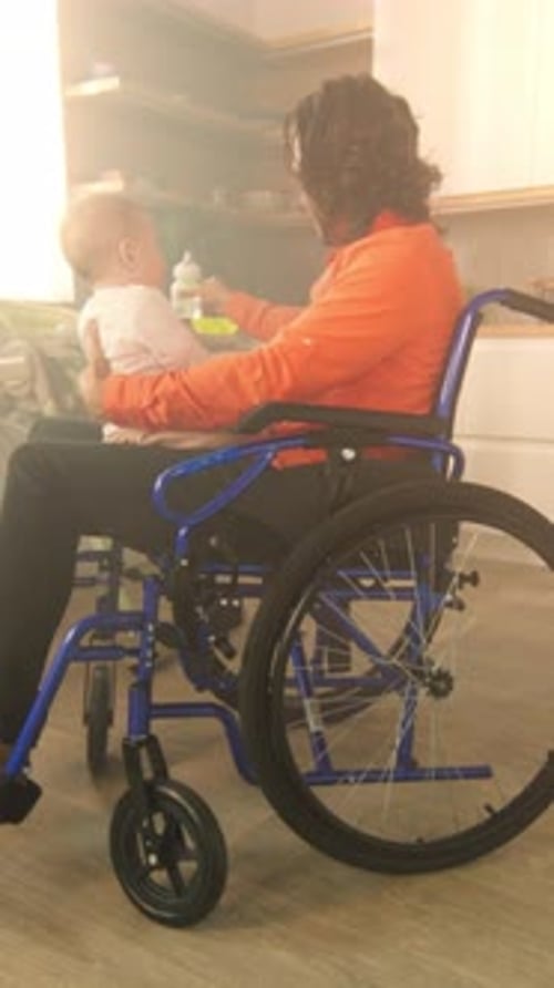Caring Man Feeds Baby in Wheelchair at Home