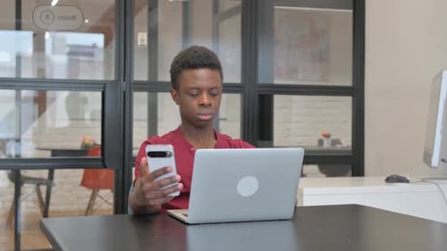 Young Man Using Laptop and Mobile Phone Indoors