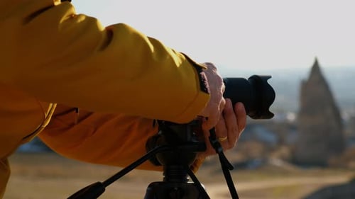 Man Adjusting Camera on Tripod in Scenic Landscape