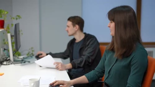 Young Positive Woman Talking to Blurred Man Sitting at Table in Office
