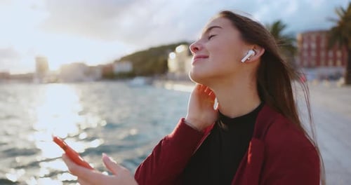 Smiling Woman with Smartphone at Sunset by Ocean