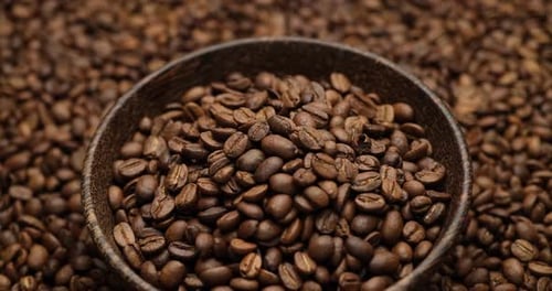 Wooden Bowl Full of Coffee Beans on a Rotating Background of Fresh Roasted Coffee Beans