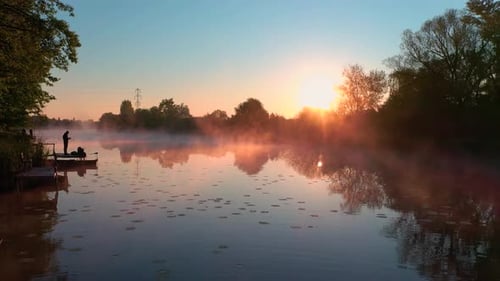 Smooth drone shot of a misty lake while the rising sun is lighting the mist