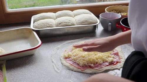 Woman making pizza at home, putting cheese on pizza.