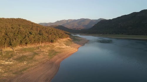Aerial drone footage following the shoreline of a beautiful lake between a picturesque mountain vall