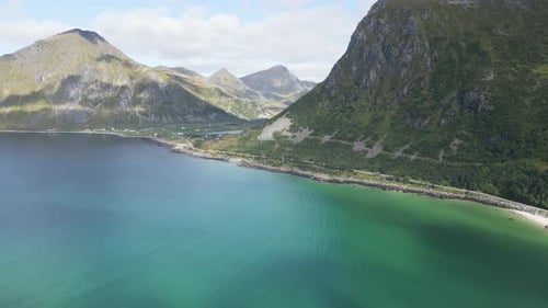 Moving camera above ocean towards mountains and above the white sand beach over the turquoise water