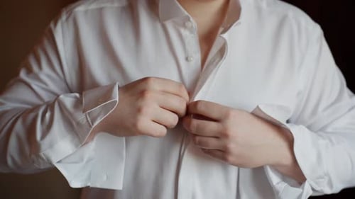 Close-up of groom buttoning his white shirt during wedding preparation