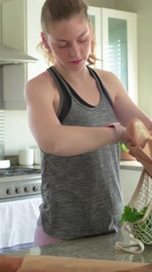 Vídeo vertical: Abriendo una bolsa de malla, una mujer tirando una manzana y descargando productos en el mostrador en un tanque gris