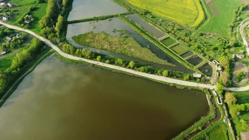 Von oben zoomt Drohnenkamera auf eine leere Landstraße zwischen ruhigen Teichen bei sonnigem Wetter