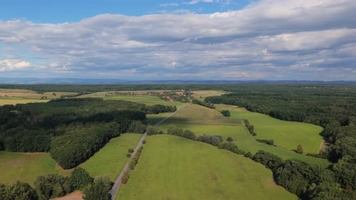 A drone view of a country road leading to a village, surrounded by fields and meadows in summer