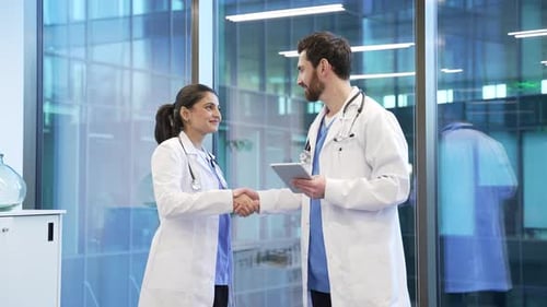 Handshake of two happy colleagues doctors at modern hospital. Two smiling medical professionals,