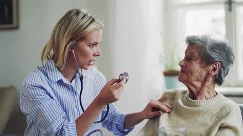 Female doctor using stethoscope to examine senior woman