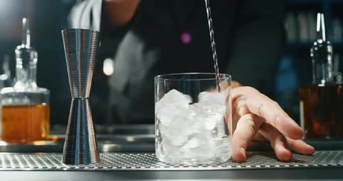 Close up of a professional bartender is preparing an alcoholic cocktail with ice cubes to customer