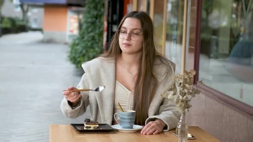 Woman Eating a Cake and Drinking Coffee in a Cafe