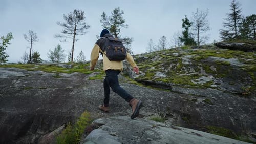 Man Hikes Up Rocky Hill in Natural Landscape
