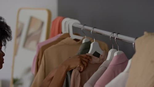 Young Woman Choosing Jacket and Blouse from Wardrobe Rack