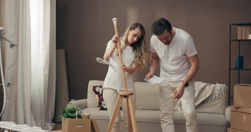Young Adorable Mother with Father Reading Instruction Trying to Assemble Decorate Furnish New Floor