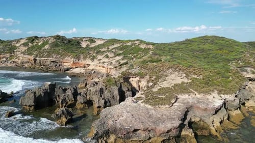 Rocky sea cliffs with big ocean waves crashing on the shore, wide aerial orbit view