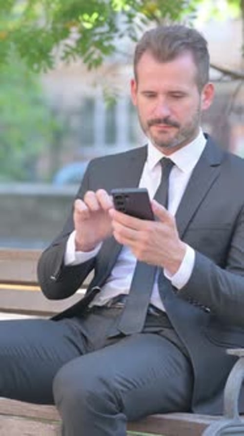 Happy Businessman Celebrates Success Using Smartphone Outdoors