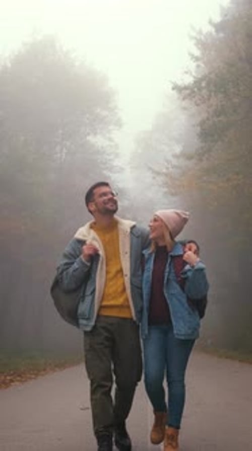 Vertical video of couple spending time together walking on forest road on a foggy morning.