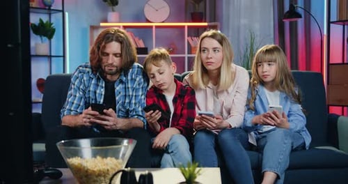 Unglücklicher Familienvater, Frau und Kinder, die ihre eigenen Telefone benutzen, da es im Fernsehen nichts zu sehen gibt