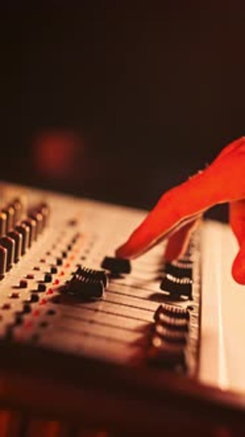 Vertical Hand Adjusts Volume Level Controls on Mixing Console Faders in Neon