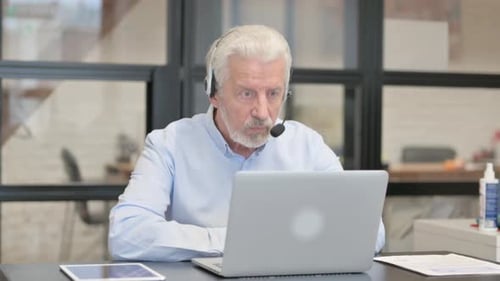 Old Man with Headset Doing Video Chat on Laptop in Call Center