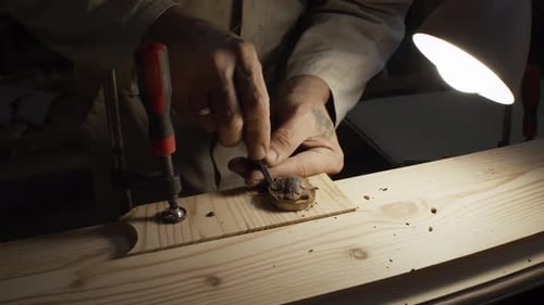 Craftsman Carefully Carving Wood at Workbench Under Lamp