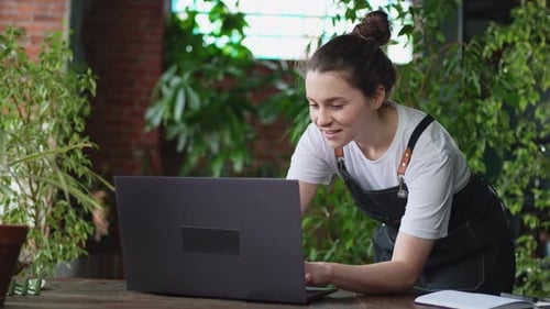Female Florist Gardener Working in Botanical Store Greenhouse Using Laptop Order Plants