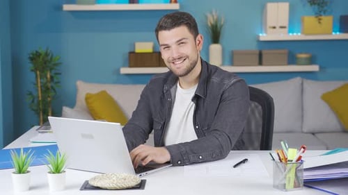 Man working from laptop smiles looking at camera.