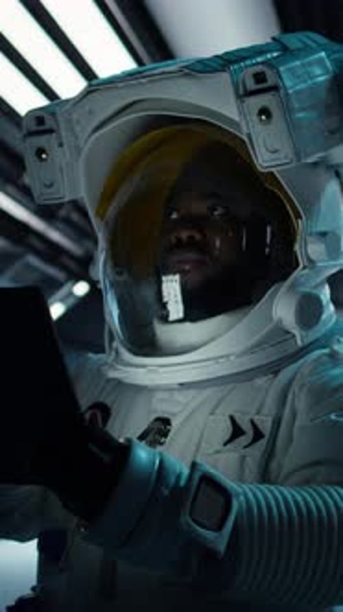 Vertical Video Astronaut Wearing Spacesuit Monitoring Mission Data on Tablet in Spacecraft