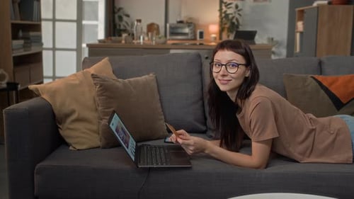 Woman Lying on Sofa Uses Laptop and Card
