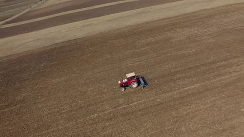Slow motion aerial view of spring agricultural field work, tractor with seeder sow seeds in ground