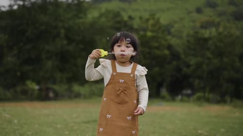 slow motion of happy toddler girl blowing soap bubbles in grass field