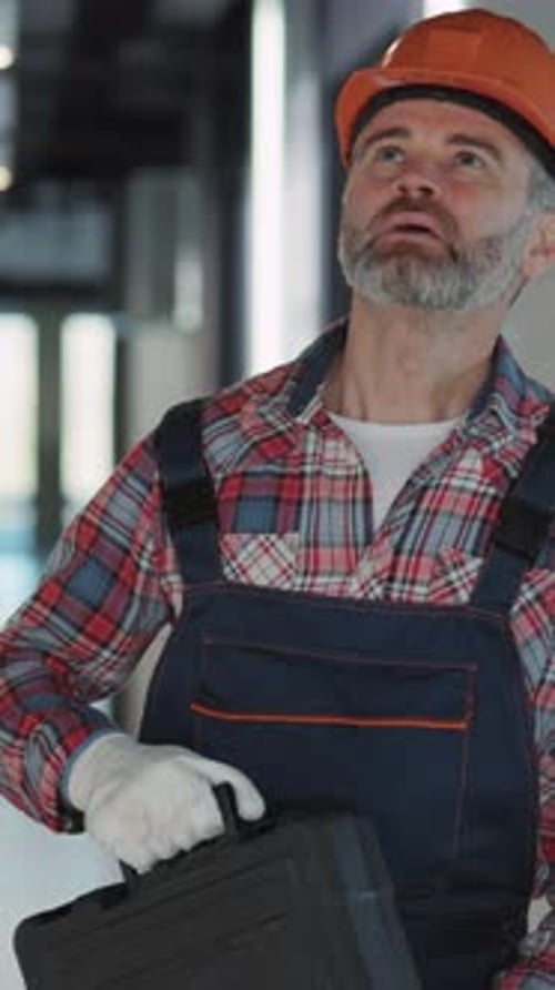 A Construction Worker Wearing a Hard Hat and Overalls is Actively Engaged in a Modern Workspace