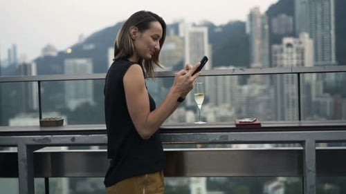 Young woman texting on smartphone in luxury skybar with a stunning city view