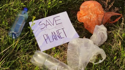 Save planet poster sign white paper on green grass polluted with waste plastic bottles and bags, pro