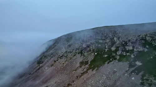Aerial shot sharp cliffs with gray rock formations and fog revealing the mountain ridge and sunrise