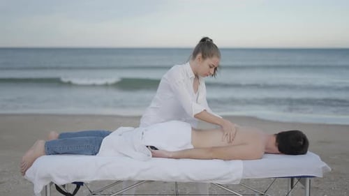 Unrecognizable Man Lies Down and Receives Relaxing Back Massage at the Beach