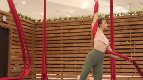 Young brunette woman in a minimal and modern gym with wooden dividers doing flying yoga with some br