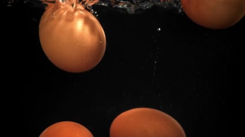 Eier, die auf schwarzem Hintergrund unter Wasser fallen, gefilmt mit einer Hochgeschwindigkeitskamera mit 1000 Bildern pro Sekunde